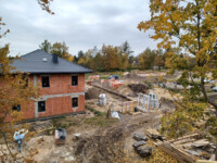 Widok na dom E i plac obok oraz fundamenty domu G